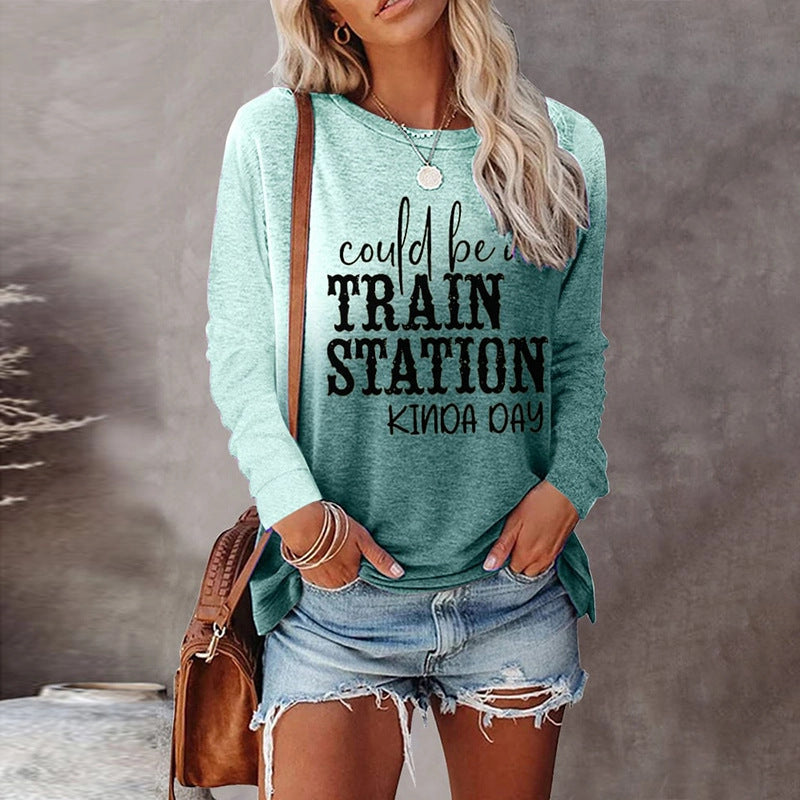 Woman wearing a teal sweatshirt with text, holding a brown bag against a neutral background